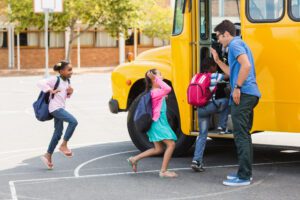 Children giving man a high five as they get on a school bus