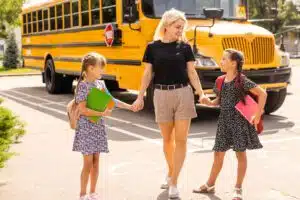 Mom holding two girls' hands as they walk away from school bus