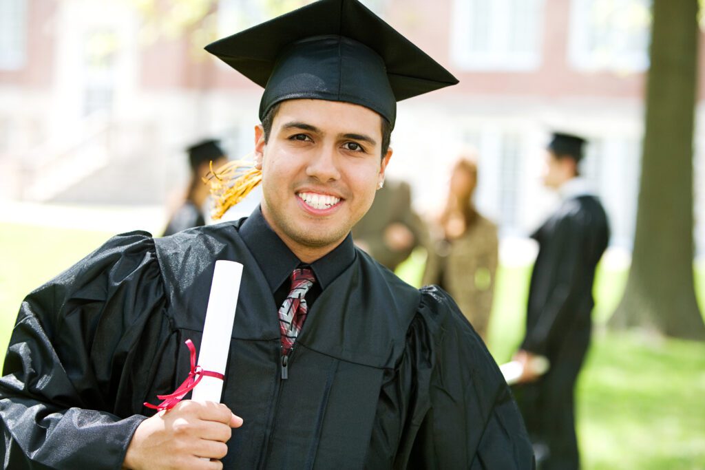 Hispanic male wearing cap and gown while holding diploma