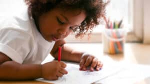 Preschool girl coloring with red crayon