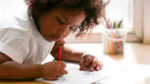 Preschool girl coloring with red crayon