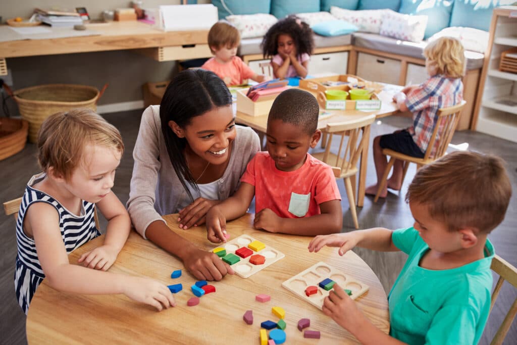 Preschool classroom; teacher helping a group of students with shape puzzles