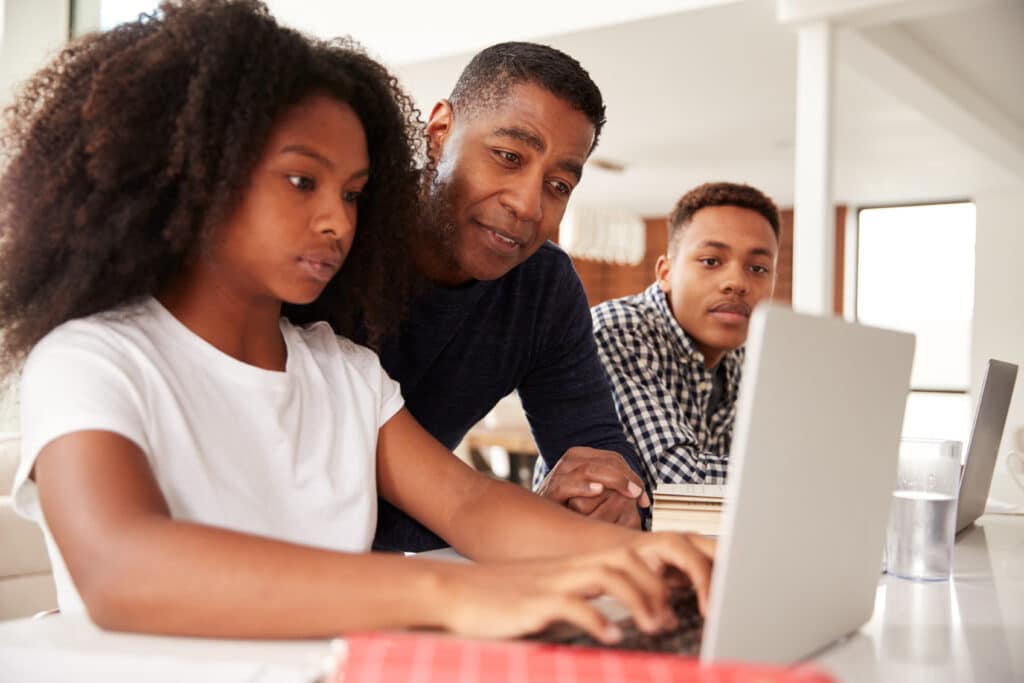 Father helping two children with homework on laptops