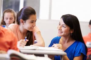 Teacher smiling at teen student at student's desk