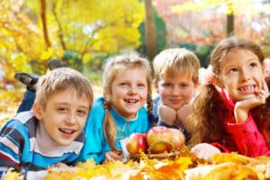 Four young children with apples and fall leaves in front of them