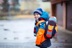 Young boy wearing coat, scarf, hat, gloves, and backpack