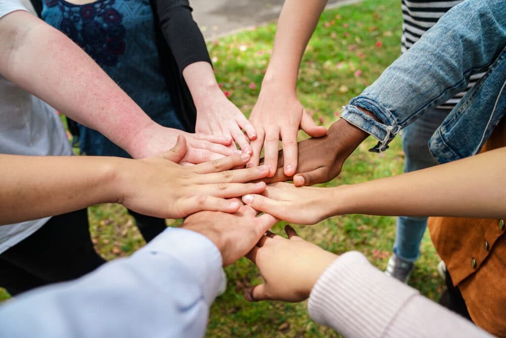 Multiracial group of people all putting their hands in a circle on top of one another