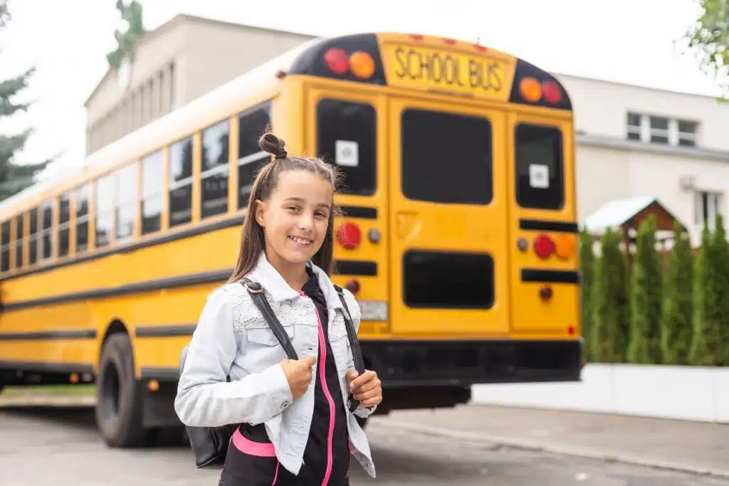 Elementary student smiling in front of a school bus